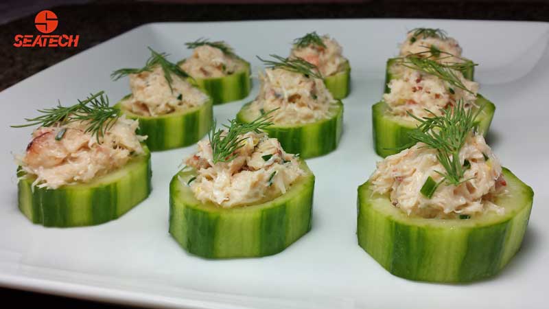 crab stuffed english cucumber bites A photograph of sliced English cucumbers stuffed with crab salad and topped with a sprig of fresh dill.